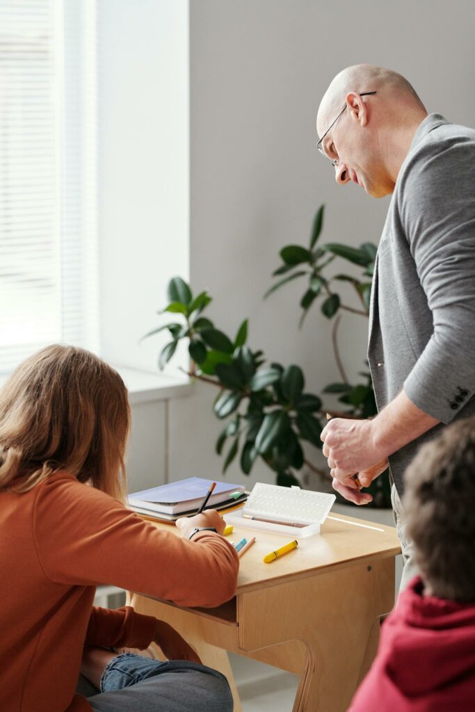 A teacher helps students during a classroom activity with books and notepads.